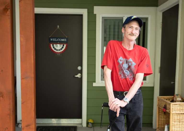 Smiling man in front of home with Welcome sign