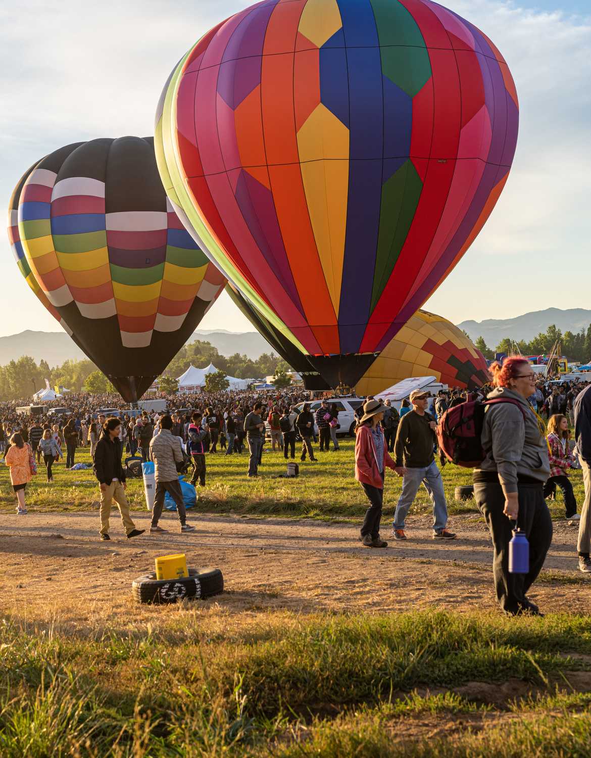 Two colorful hot air balloons are tethered to the ground, surrounded by crowds of people at the Great Reno Balloon Race.
